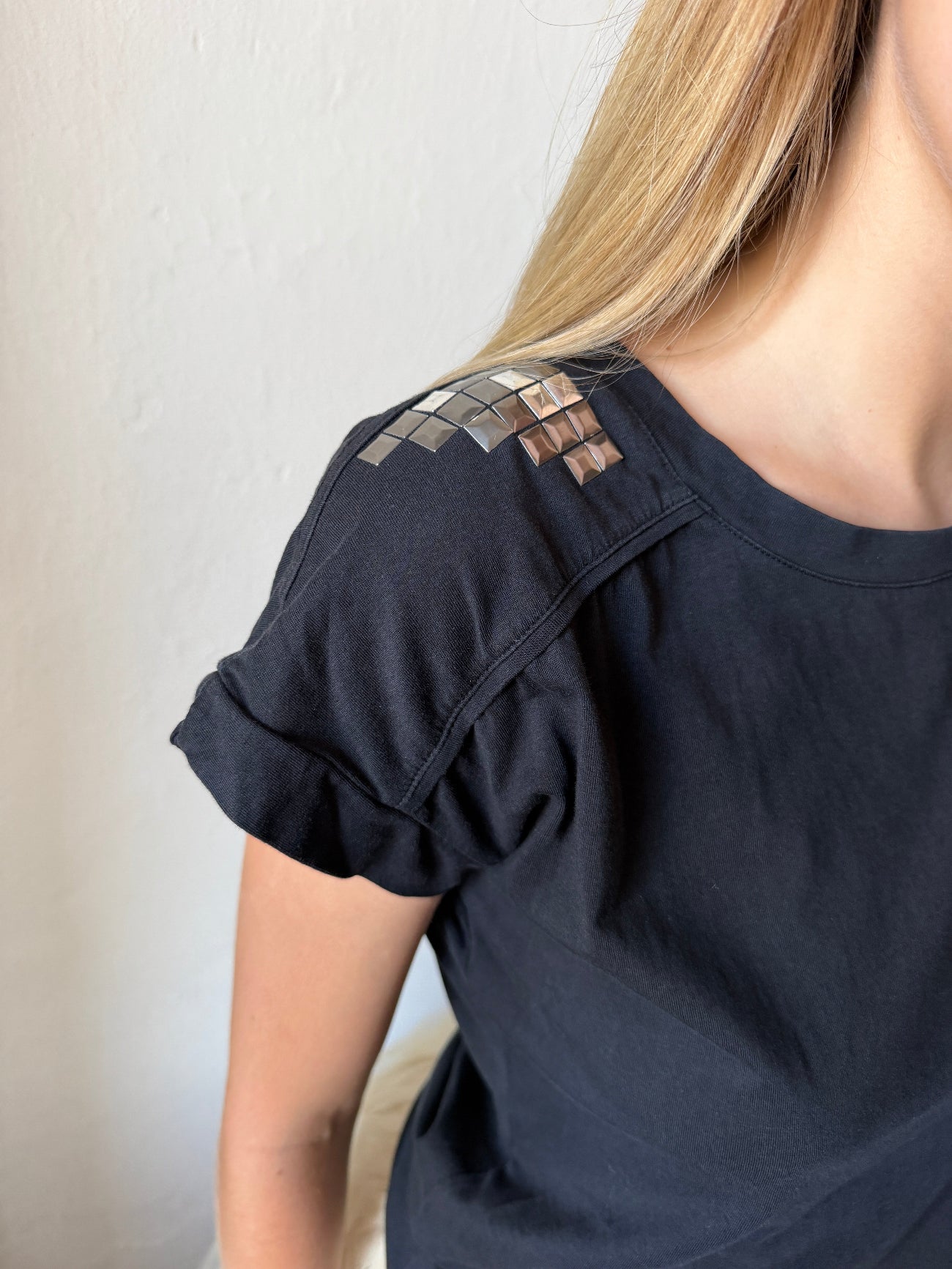 model wearing a black  short-sleeve top with a geometric metallic pattern detail on the shoulder