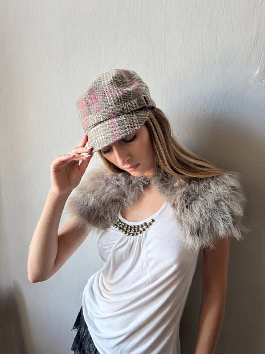 model wearing a gray and pink plaid newsboy cap, a fluffy gray faux-fur collar, and a white top