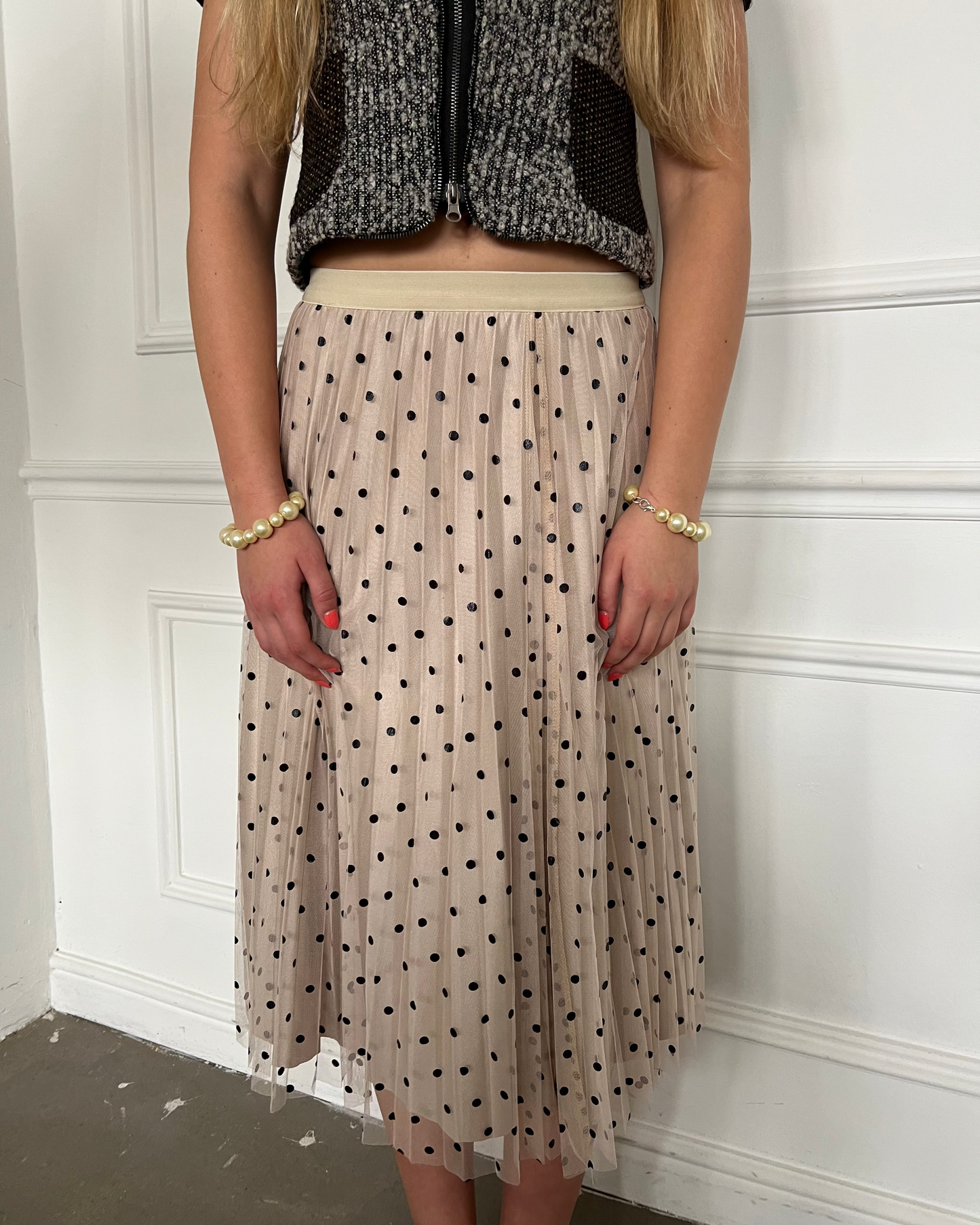 Person wearing a polka dot skirt and textured top against a white wall.